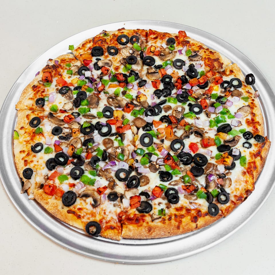 Vegetable pizza topped with black olives, mushrooms, bell peppers, tomatoes, onions, and melted cheese on a metal tray.