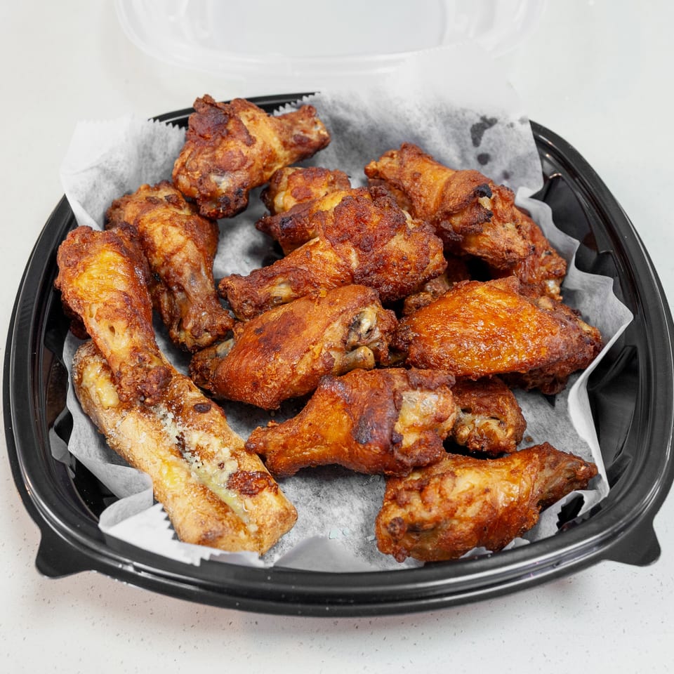 Crispy golden-brown fried chicken wings and drumettes arranged in a black takeout tray lined with parchment paper.
