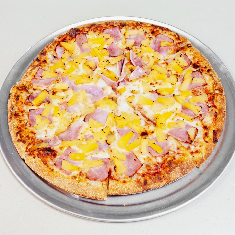 Hawaiian pizza topped with ham and pineapple on a round metal serving tray.