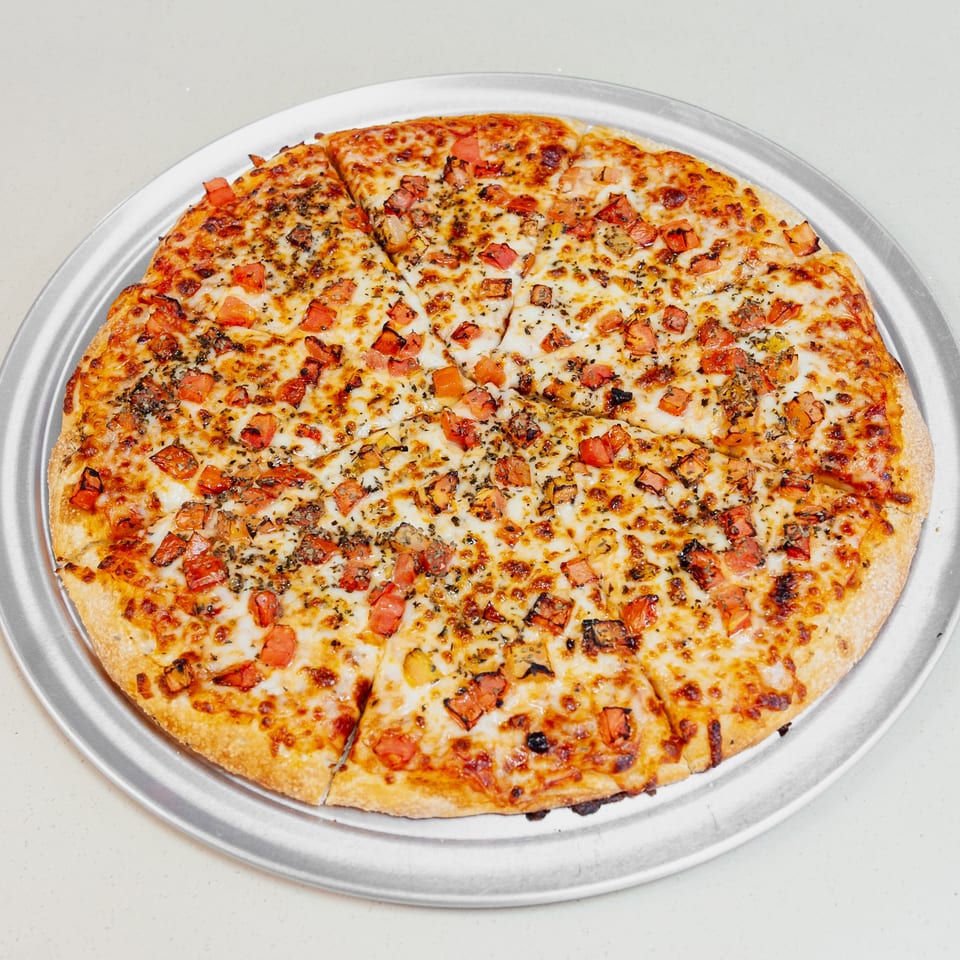 Large cheese pizza topped with diced tomatoes and herbs, sliced into pieces on a silver serving tray.